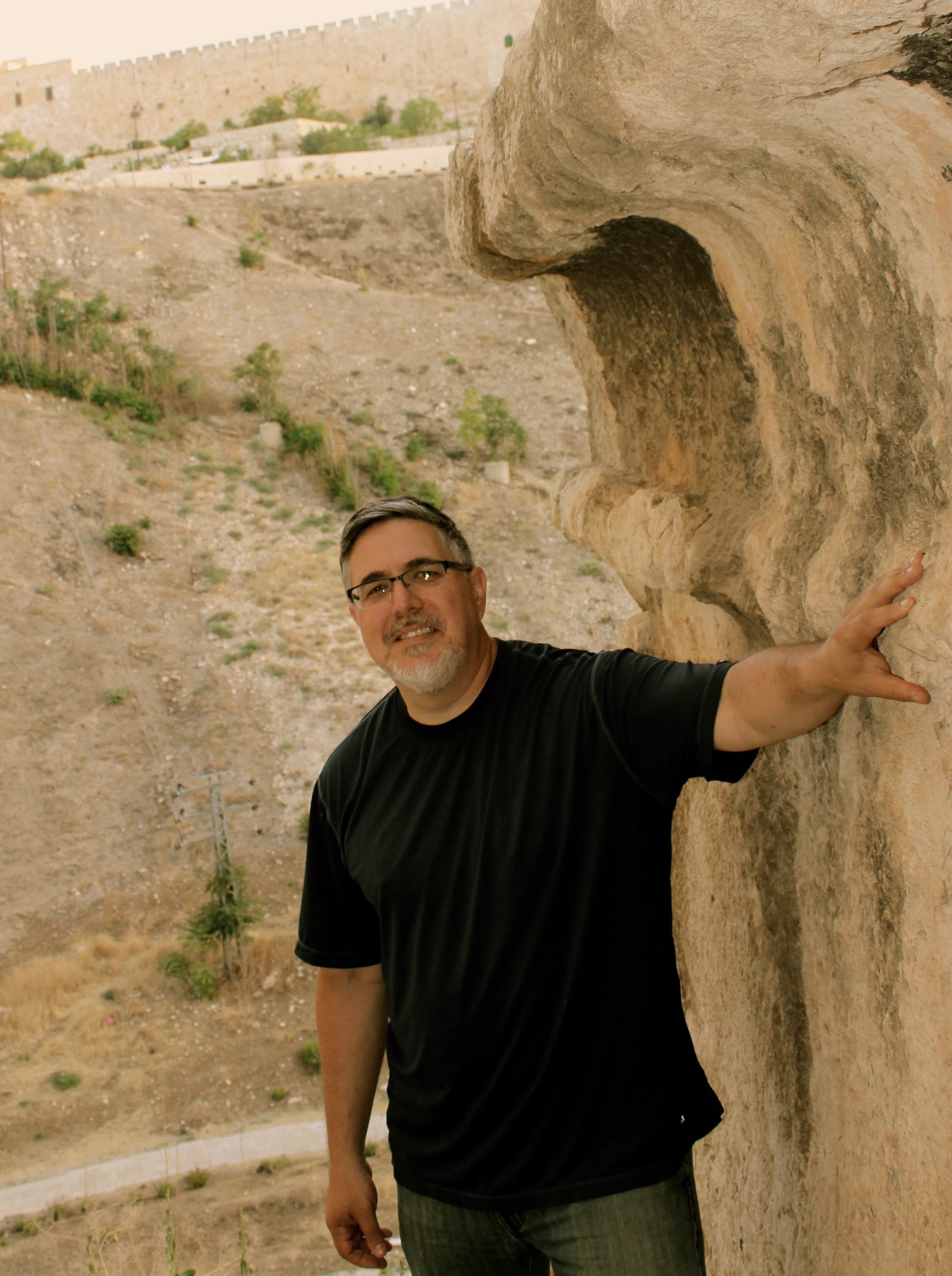 Professor Suriano standing next to a monolithic-tomb in Jerusalem. The tomb's cornice is visible above him and in the background is the Kidron Valley.