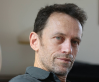 Headshot photo of Alex Weintraub against a gray with black background. 