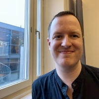 Head pic of Matthew Johnson near a window with a view of a building with rails 